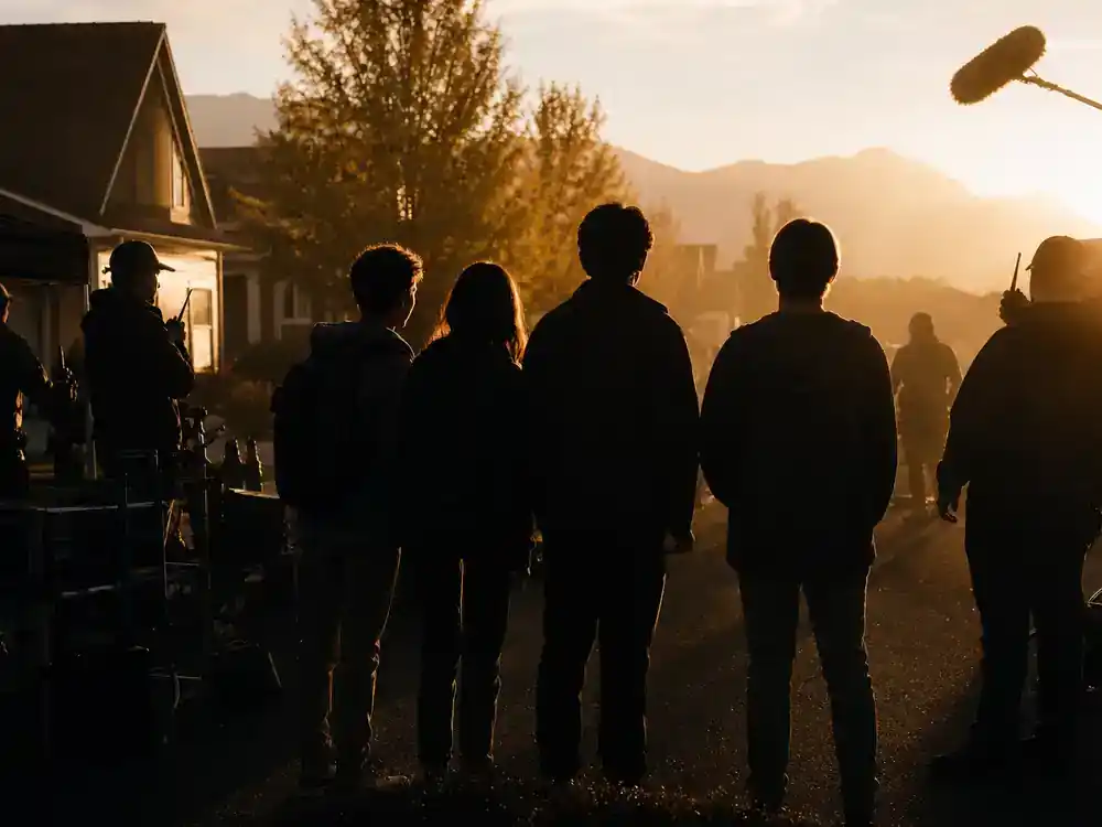 A Minecraft Movie cast and cameos guide misfits ensemble — four young actor silhouettes blocking suburban Idaho location scene with crew walkie-talkies