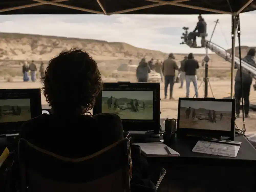 A Minecraft Movie cast and cameos guide Jared Hess — director silhouette reviewing monitors at outdoor video village tent with clapperboard on table