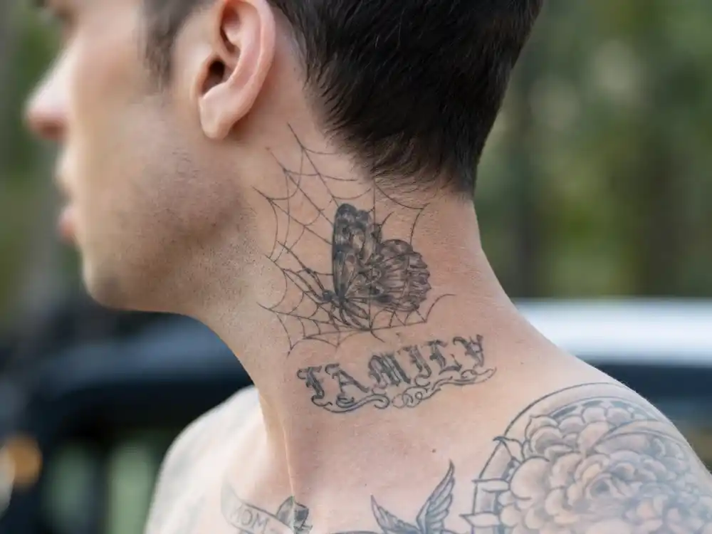 Adam Levine tattoo collection guide neck butterfly — side profile blurred singer showing spiderweb butterfly throat tattoo and family collarbone script