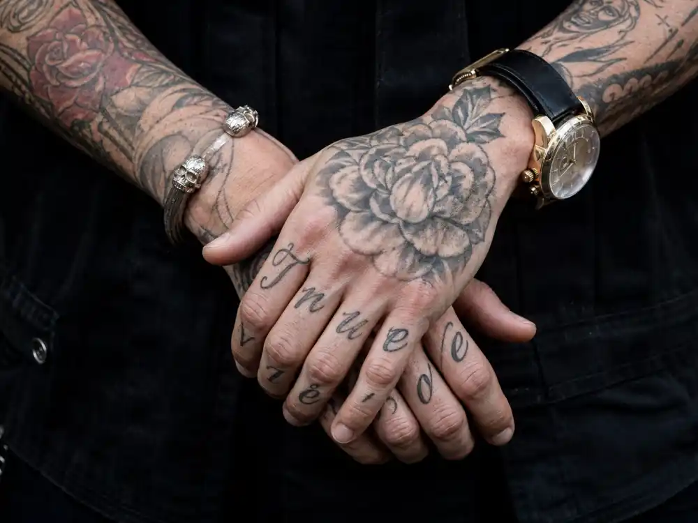 Adam Levine tattoos and their meanings arm ink — close-up of True Love finger script and floral hand tattoos on forearms