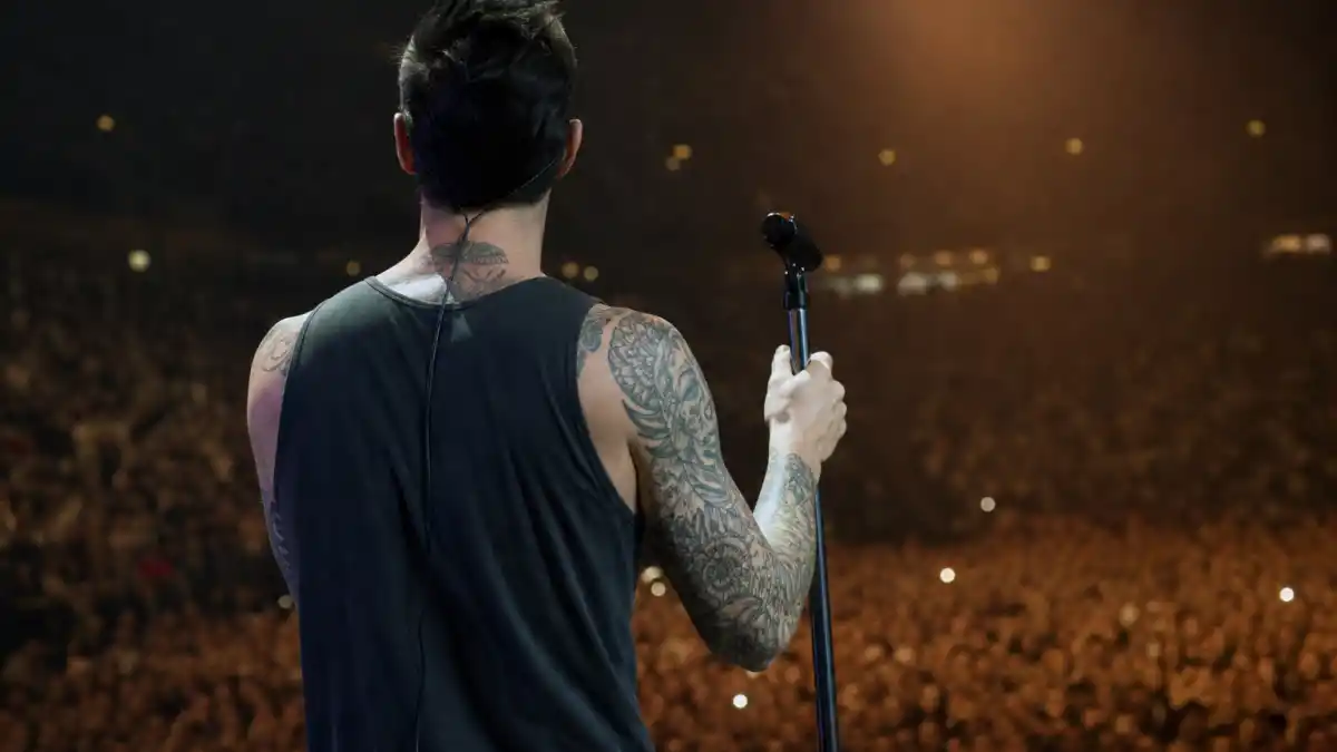 Adam Levine tattoos and their meanings — lean Maroon 5 frontman from behind showing arm sleeve and neck ink on concert stage