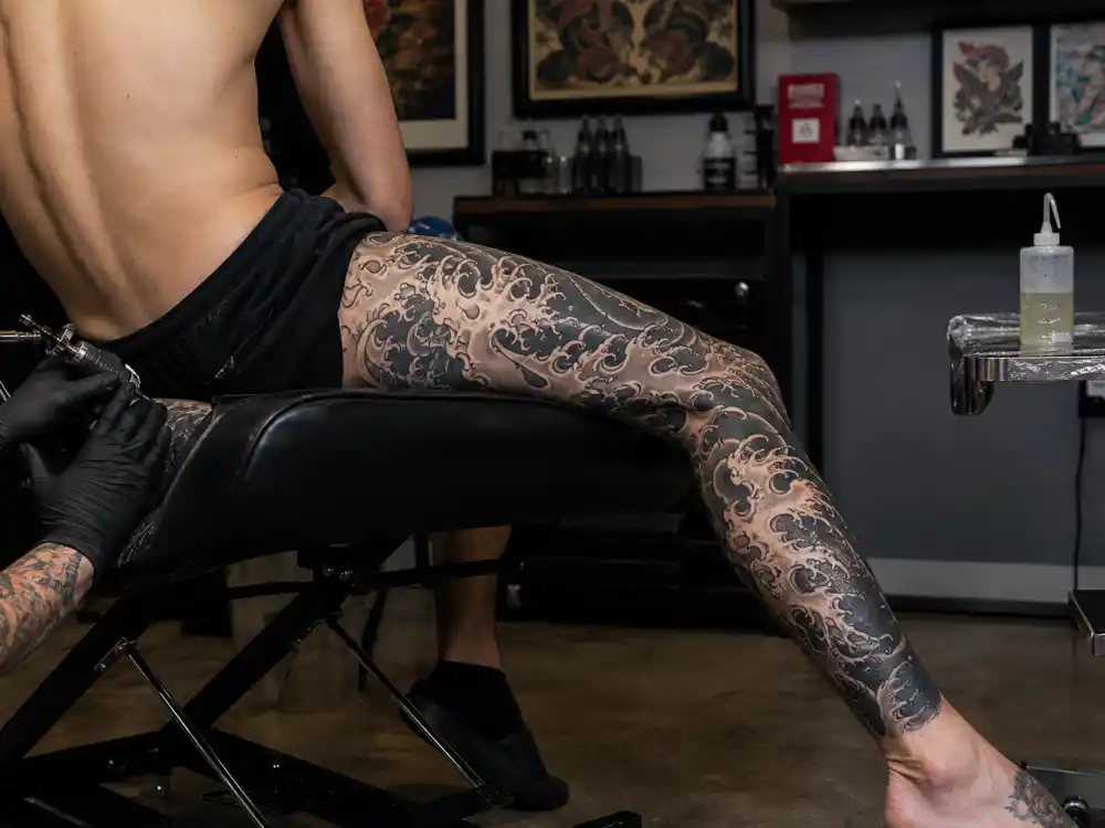 Adam Levine tattoos and their meanings leg sleeve — full Japanese wave tattoo on left leg in studio session from behind
