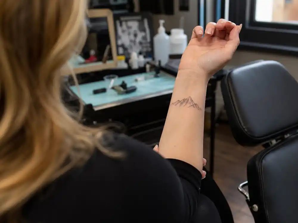 Adele tattoos and their meanings mountain — Dr Woo single-needle black and grey mountain range tattoo on left wrist at Shamrock Social Club