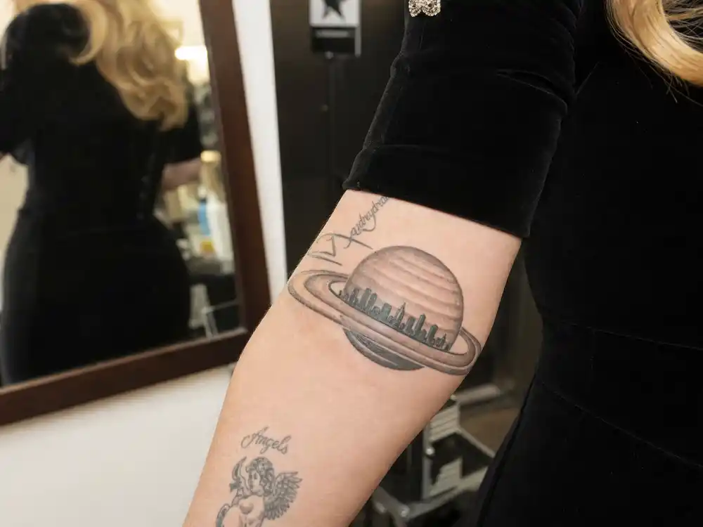 Adele tattoos and their meanings Saturn — planet Saturn tattoo with Los Angeles skyline inside ring on right wrist backstage at London venue