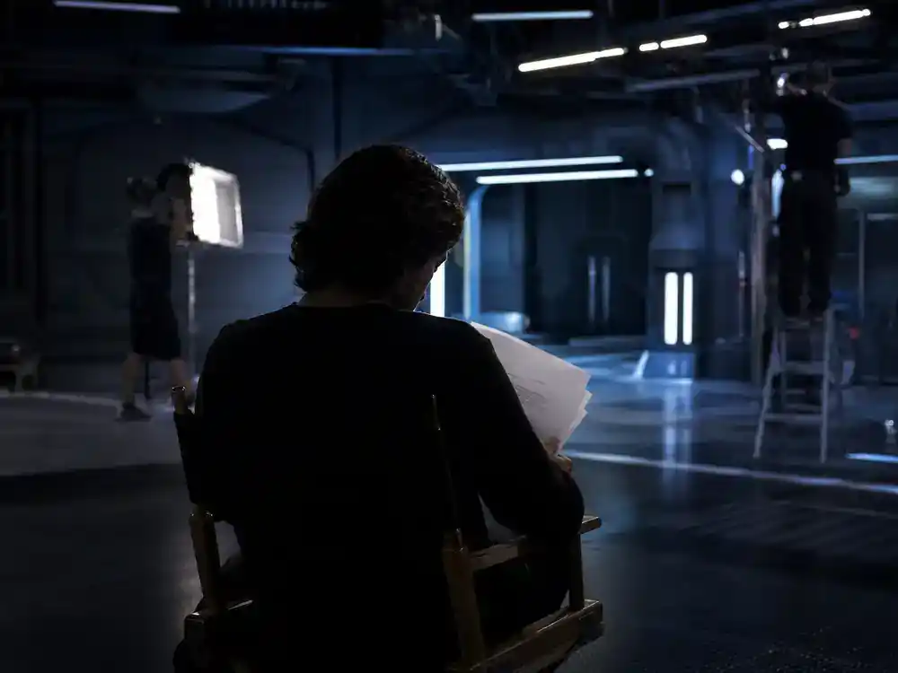 Andor season 2 cast and Star Wars timeline guide Diego Luna Cassian — actor silhouette from behind on director chair reviewing script at sci-fi production set