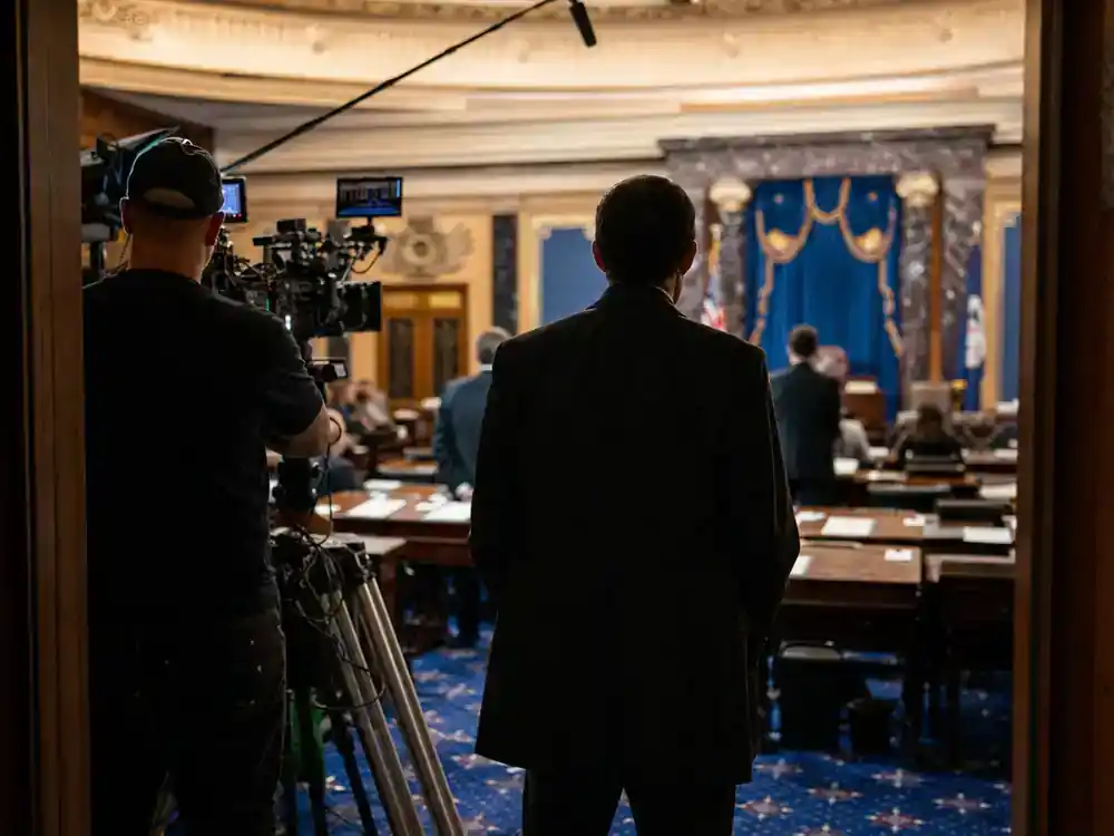 Andor season 2 cast and Star Wars timeline guide Genevieve O'Reilly Mon Mothma — actor silhouette from behind in formal senate chamber film set with marble columns