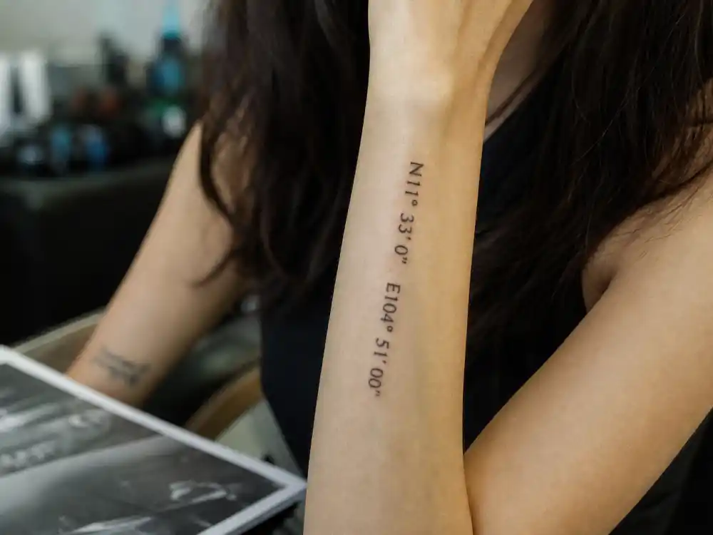 Angelina Jolie tattoos and their meanings — close-up of latitude and longitude coordinate tattoos on left forearm marking children birthplaces