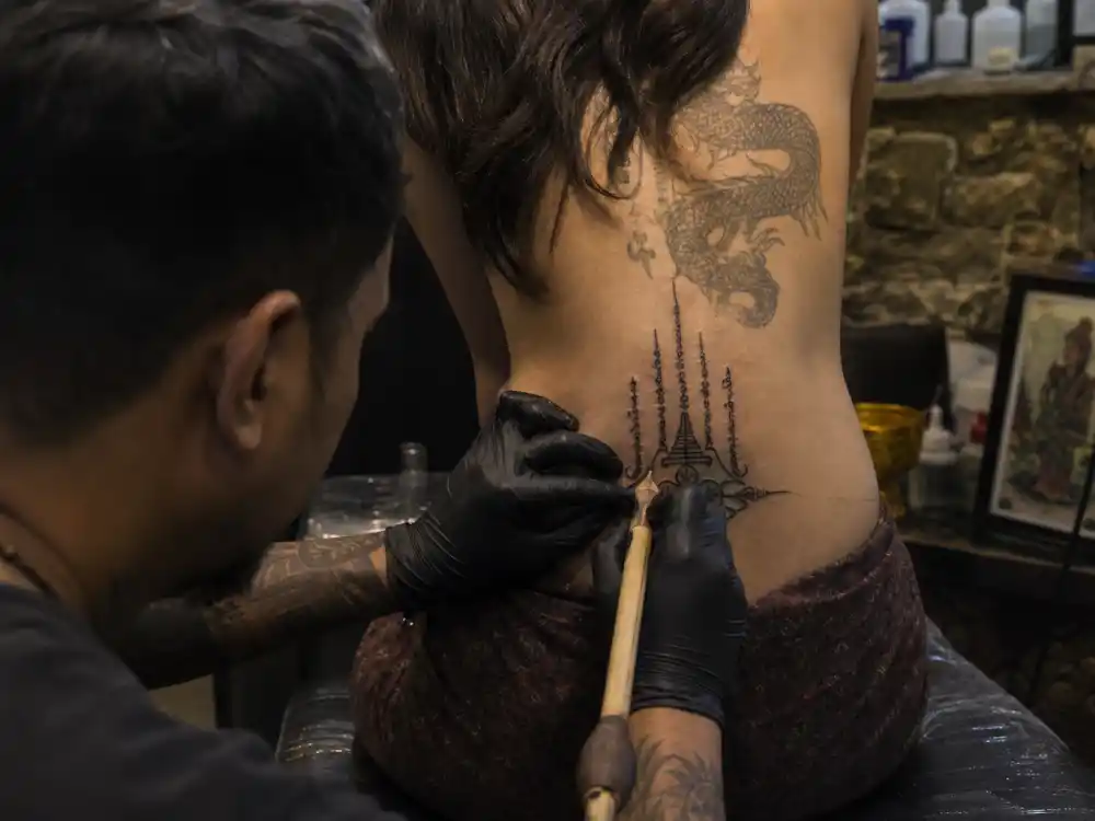 Angelina Jolie tattoos and their meanings — tattoo artist applying traditional Thai bamboo needle sak yant during Bangkok studio session