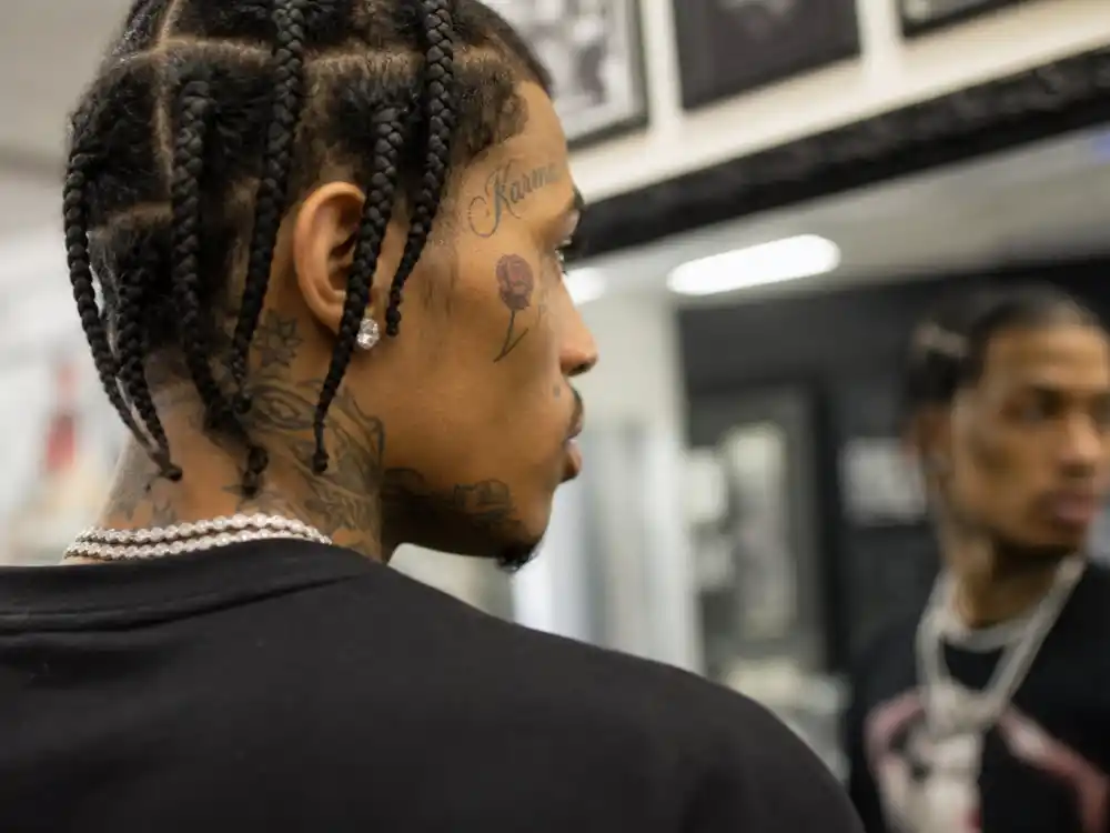 ASAP Rocky tattoos and their meanings — rose cheek tattoo and temple script visible in side profile mirror reflection