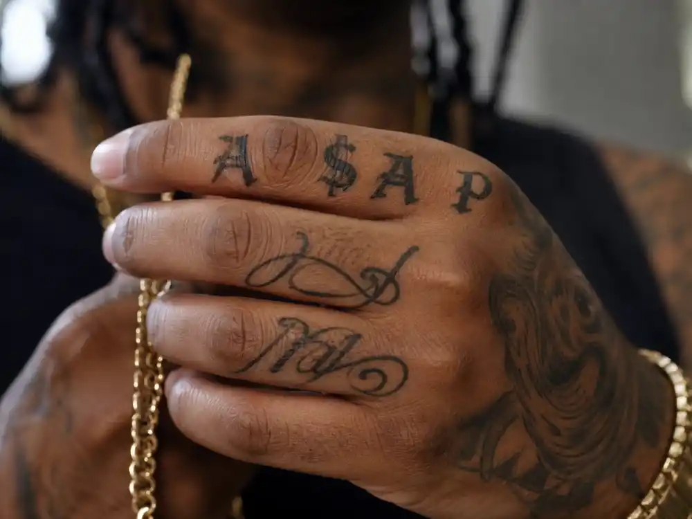 ASAP Rocky tattoos and their meanings — close-up of A$AP Worldwide script and finger lettering on rapper hand holding gold chain