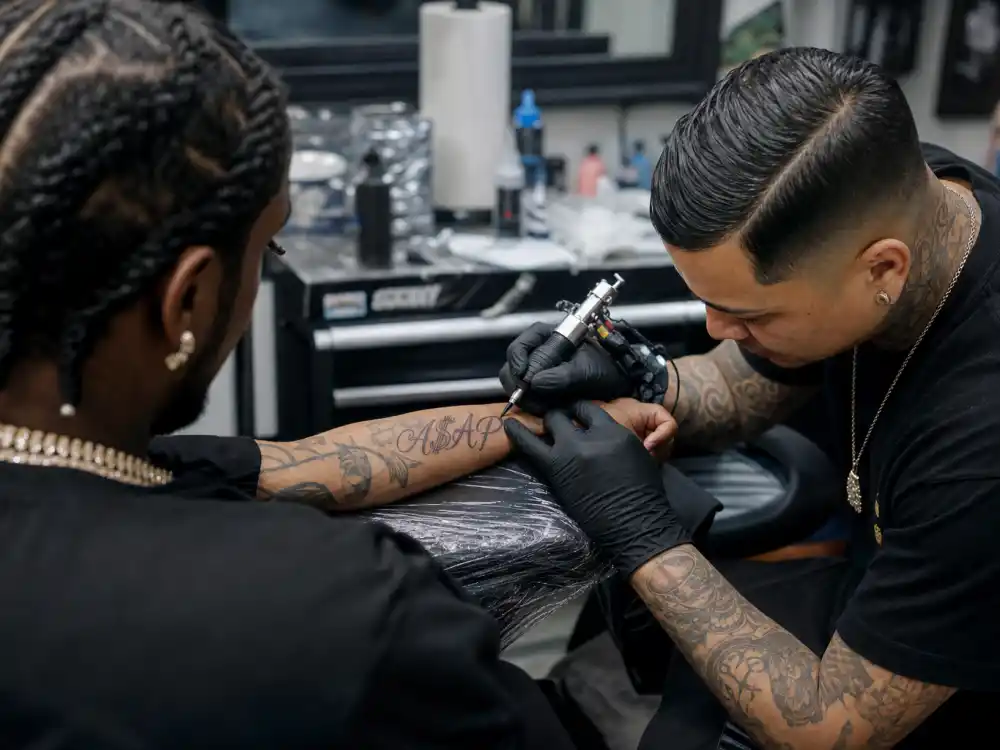 ASAP Rocky tattoos and their meanings — tattoo artist inking A$AP script lettering on rapper forearm during professional studio session