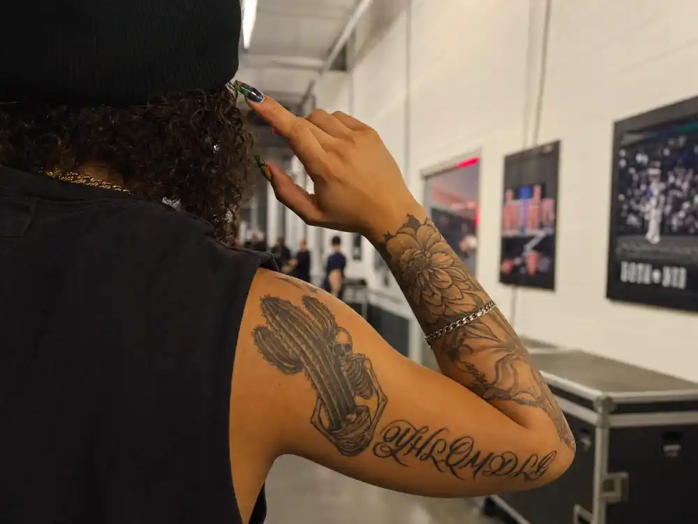 Bad Bunny tattoos and their meanings — cactus skeleton, floral bloom, and YHLQMDLG script arm tattoos over-shoulder backstage view