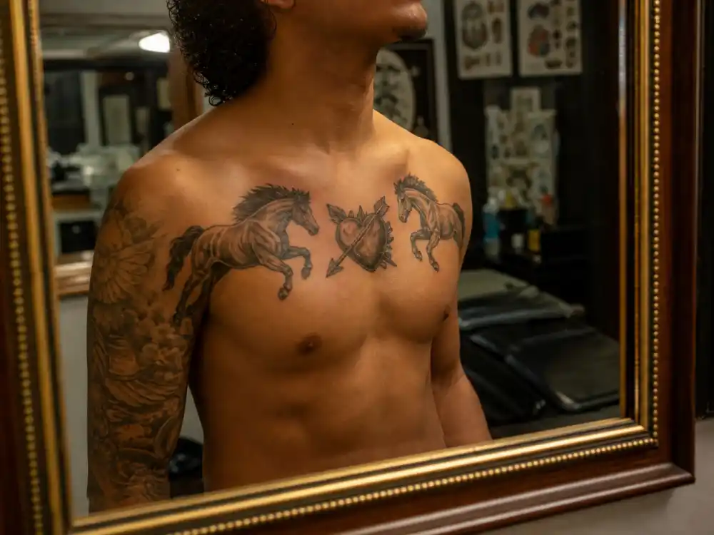 Bad Bunny tattoos and their meanings — chest heart pierced by arrow between two running horses tattoo visible in mirror reflection