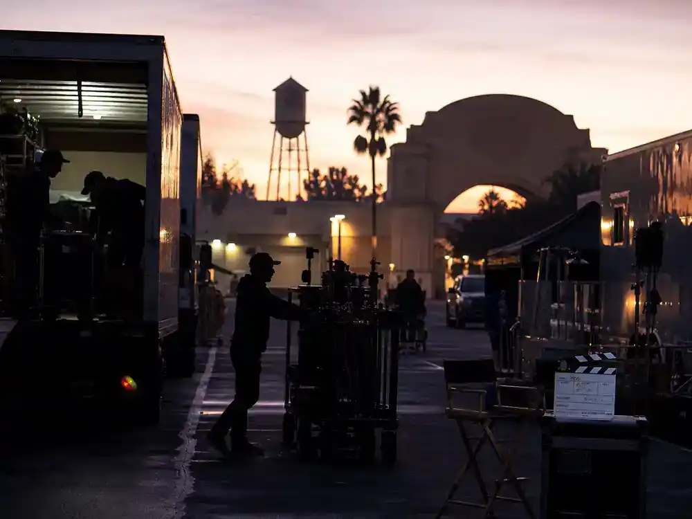 Barbie movie filming locations and set design Leavesden studio — UK film lot production trucks and crew unloading camera equipment at dawn on blockbuster shoot