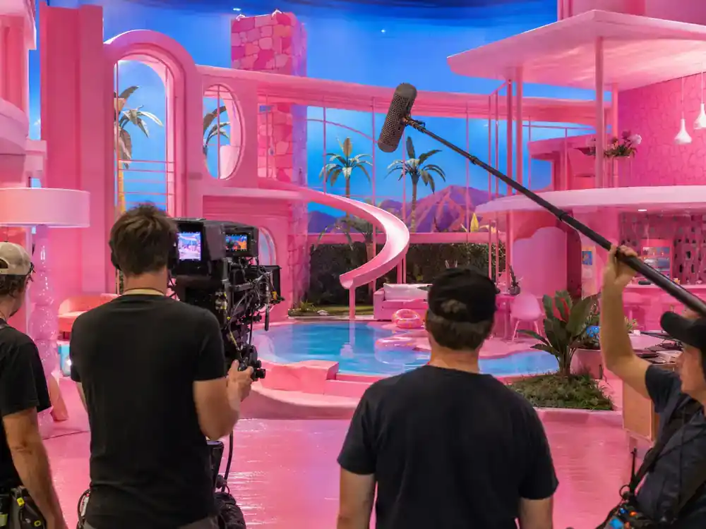 Barbie movie filming locations and set design Dreamhouse — wide pink and blue fantasy film set interior with pool slide props and camera crew filming from behind
