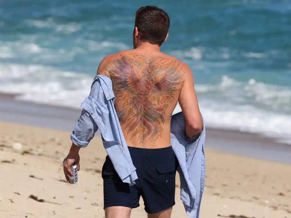 Ben Affleck tattoos and their meanings — paparazzi beach photo showing full phoenix back tattoo from behind