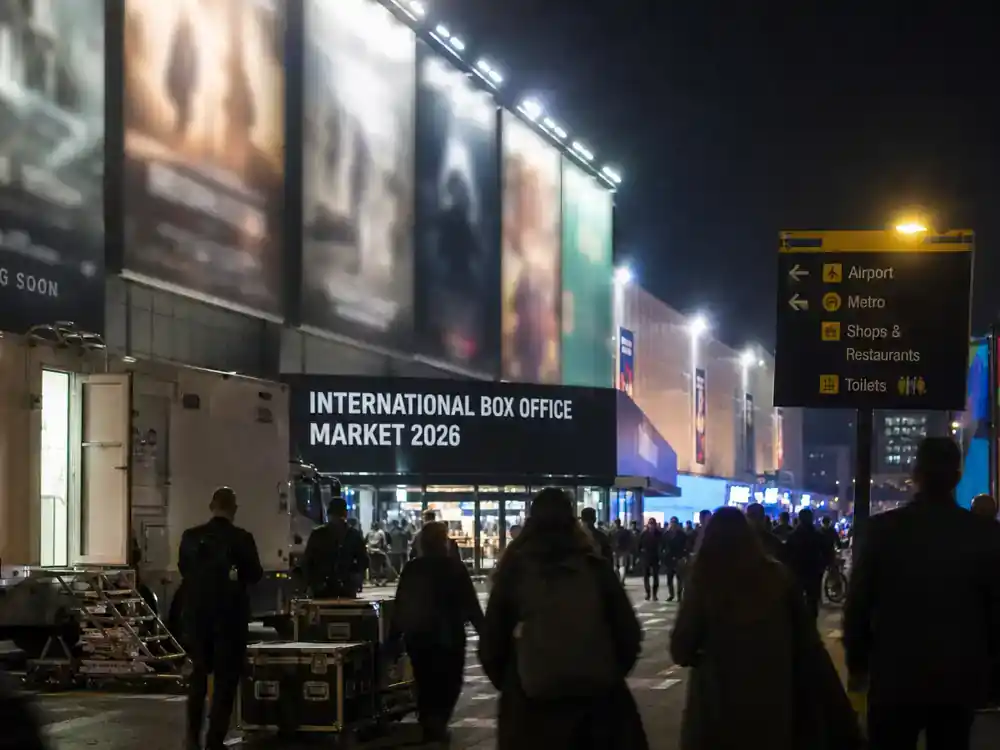 Biggest box office movies of 2026 so far international box office — cinema billboard district at night with crowd silhouettes and film production trucks