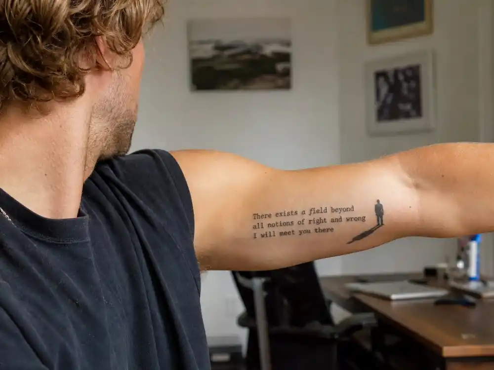 Brad Pitt tattoos and their meanings Rumi poem — inner bicep script reading there exists a field beyond right and wrong with man and shadow silhouette