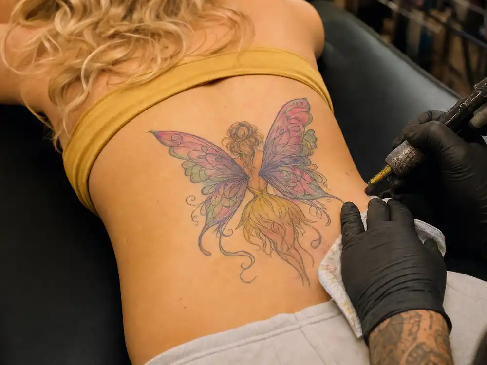 Britney Spears tattoos and their meanings fairy lower back — pink and yellow winged fairy tattoo from 2000