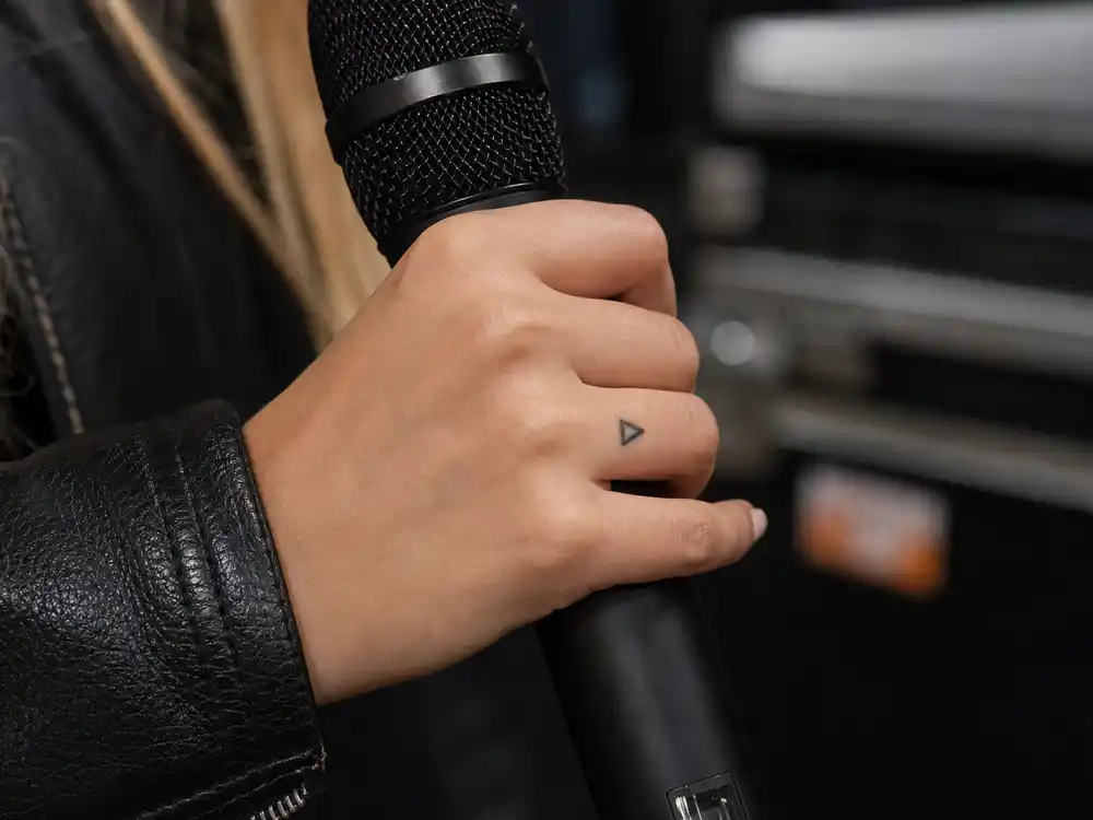 Britney Spears tattoos and their meanings triangle hand — tiny black triangle between thumb and index finger
