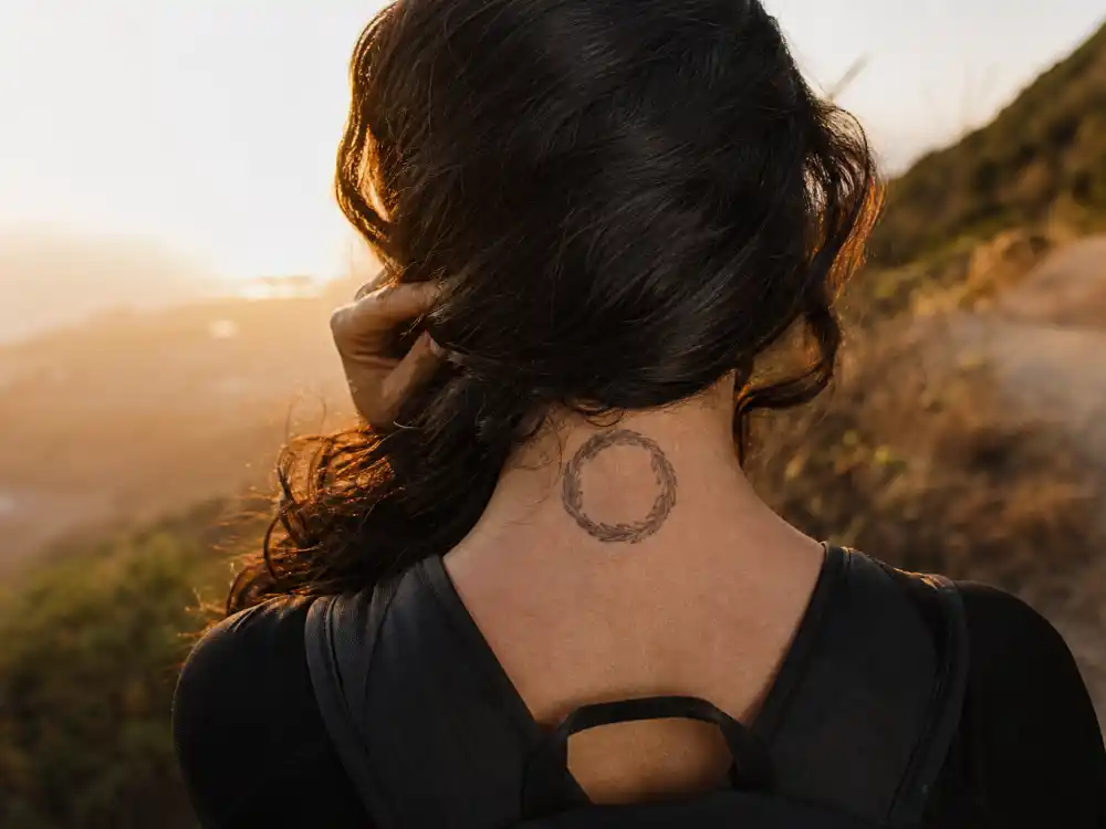 Camila Cabello tattoos and their meanings sweetgrass — braided sweetgrass circle tattoo on back of neck hiking trail over-shoulder angle