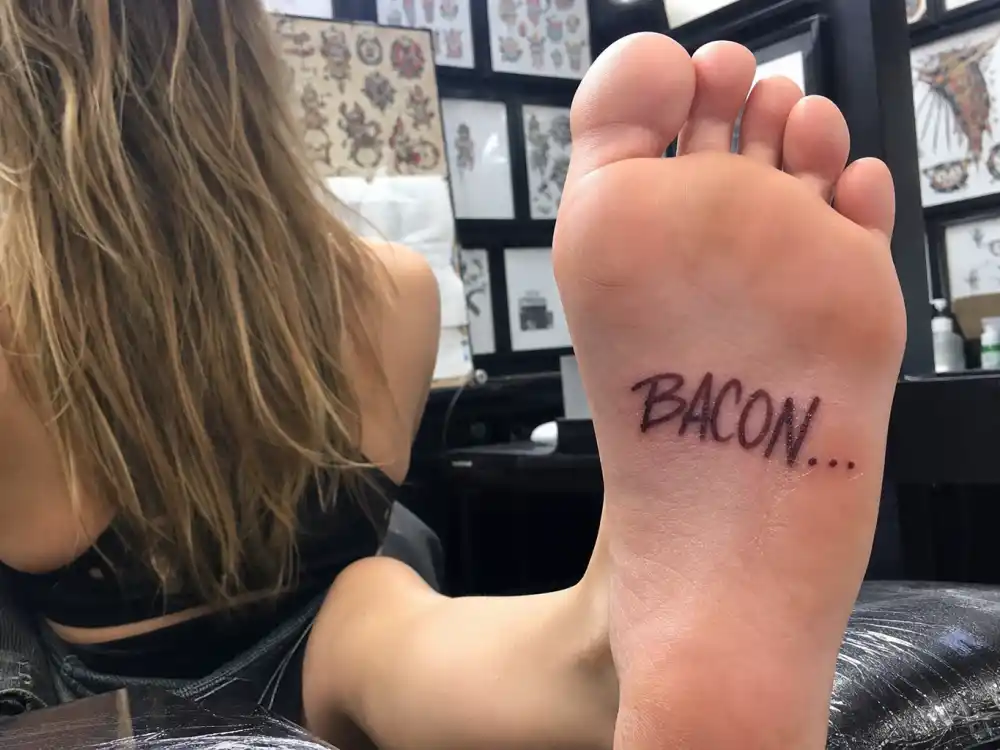 Cara Delevingne tattoos and their meanings — bacon script tattoo on bottom of left foot with Made in England foot ink