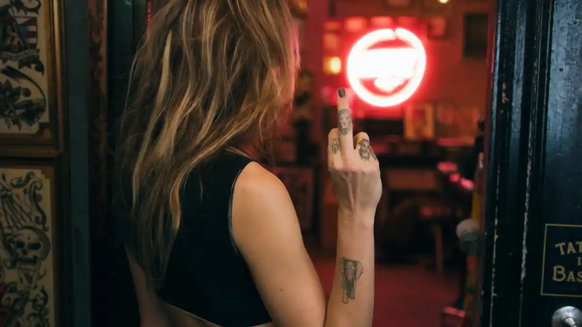 Cara Delevingne tattoos and their meanings — blonde model from behind in tattoo studio doorway with lion finger tattoo and elephant forearm ink visible