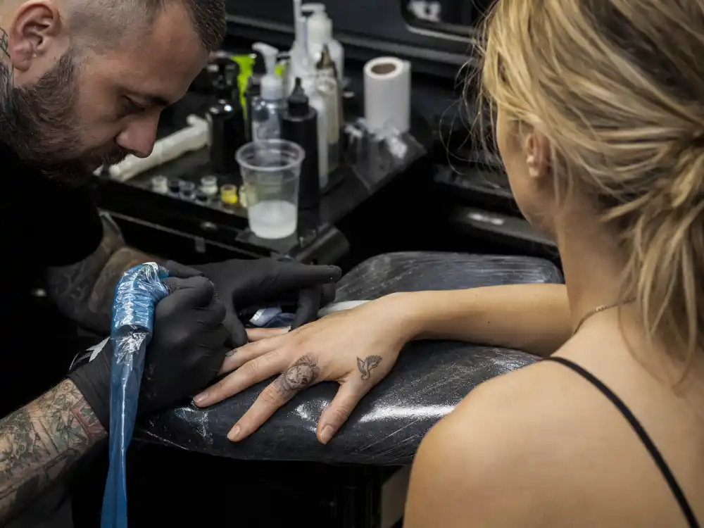 Cara Delevingne tattoos and their meanings — tattoo artist inking forearm during Bang Bang NYC studio session with lion and elephant tattoos visible