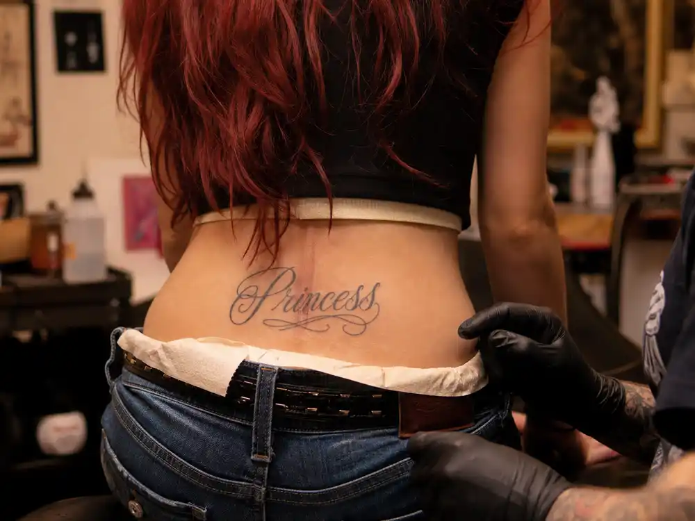 Chappell Roan tattoos and their meanings Princess — cursive Princess script lower-back tattoo close-up at tattoo studio