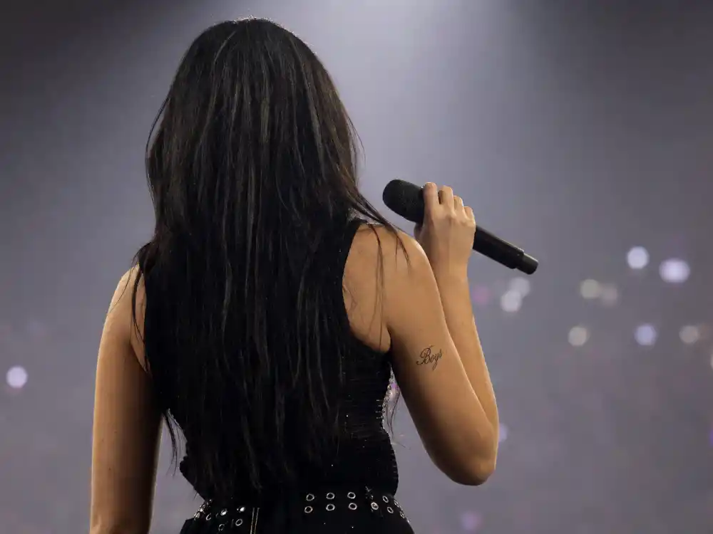 Charli XCX tattoos and their meanings — Boys arm tattoo visible during live concert performance from behind on stage