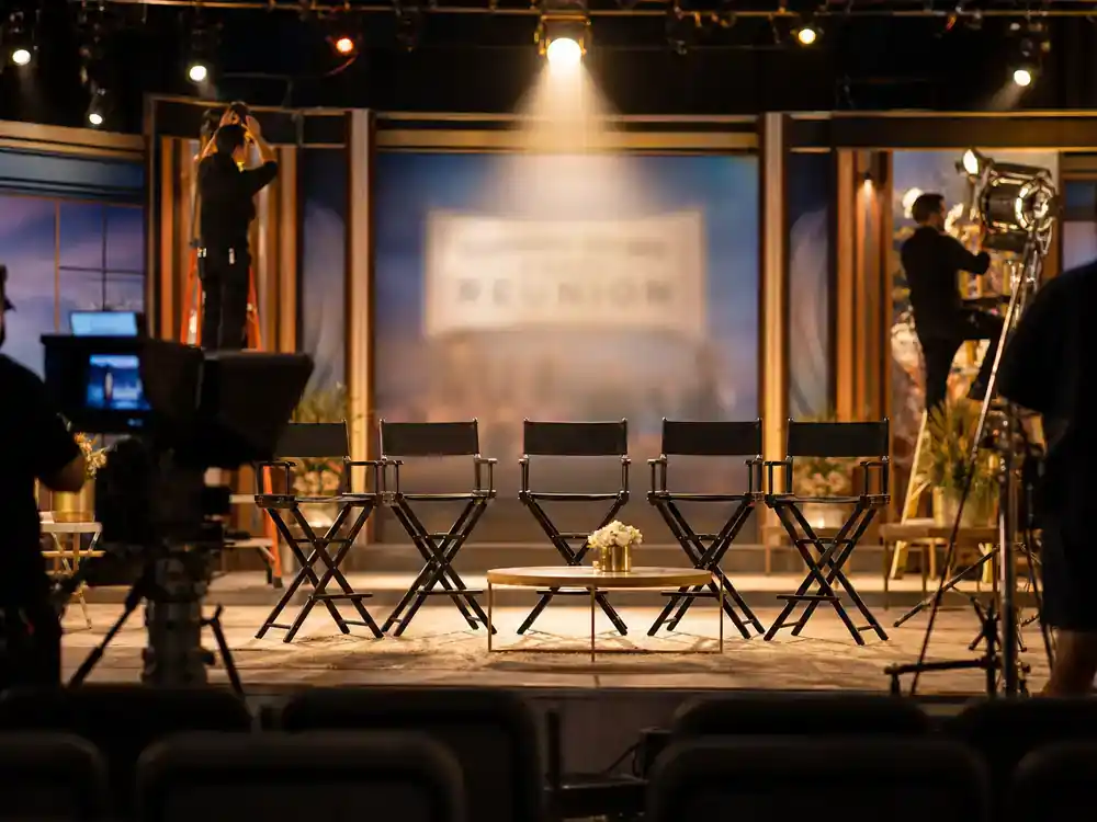 child actors from 90s sitcoms cast reunion guide reunion specials — TV reunion filming setup with director chairs facing camera and crew silhouettes adjusting studio lights