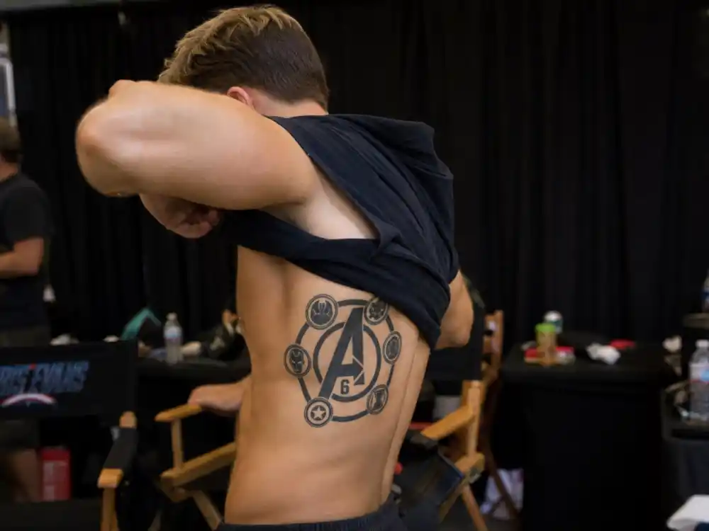 Chris Hemsworth tattoos and their meanings Avengers logo — matching Marvel cast tattoo on right rib cage with number 6 and letter A visible from behind