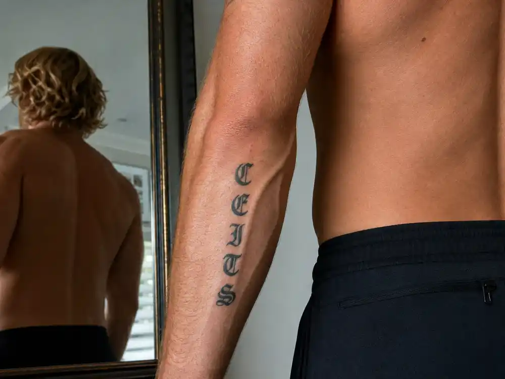 Chris Hemsworth tattoos and their meanings CEITS initials — vertical C E I T S family letters on right outer forearm of blond athletic man in mirror reflection