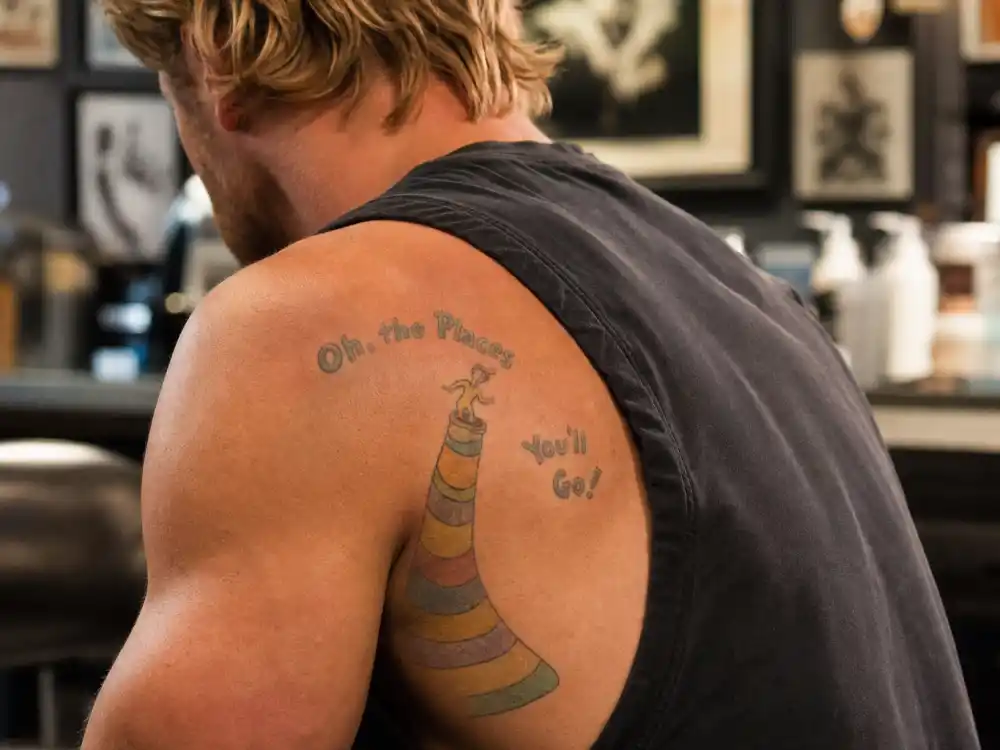 Chris Hemsworth tattoos and their meanings Dr. Seuss — left bicep Oh the Places Youll Go character tattoo partially faded on muscular blond arm over-shoulder angle