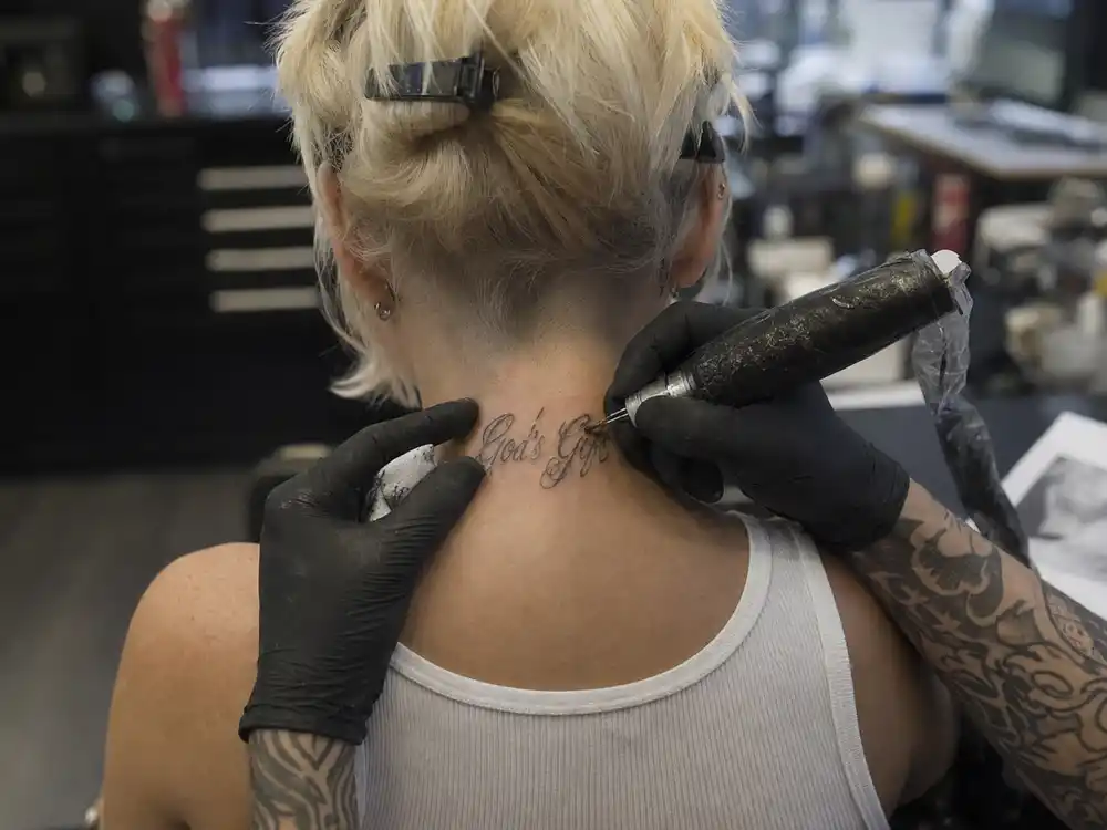 Christina Aguilera tattoos and their meanings studio session — tattoo artist applying neck script to platinum blonde pop star from behind