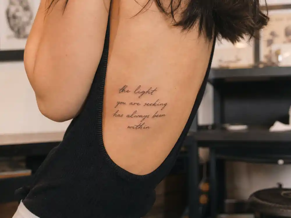 Christina Ricci tattoos and their meanings — Move or Bleed script lettering tattoo along rib cage from over-shoulder angle