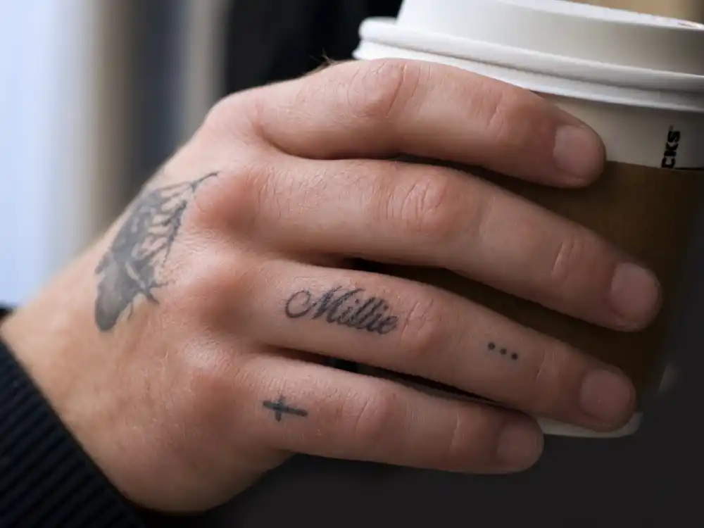 Colin Farrell tattoos and their meanings — Millie ring-finger script tattoo on hand close-up backstage
