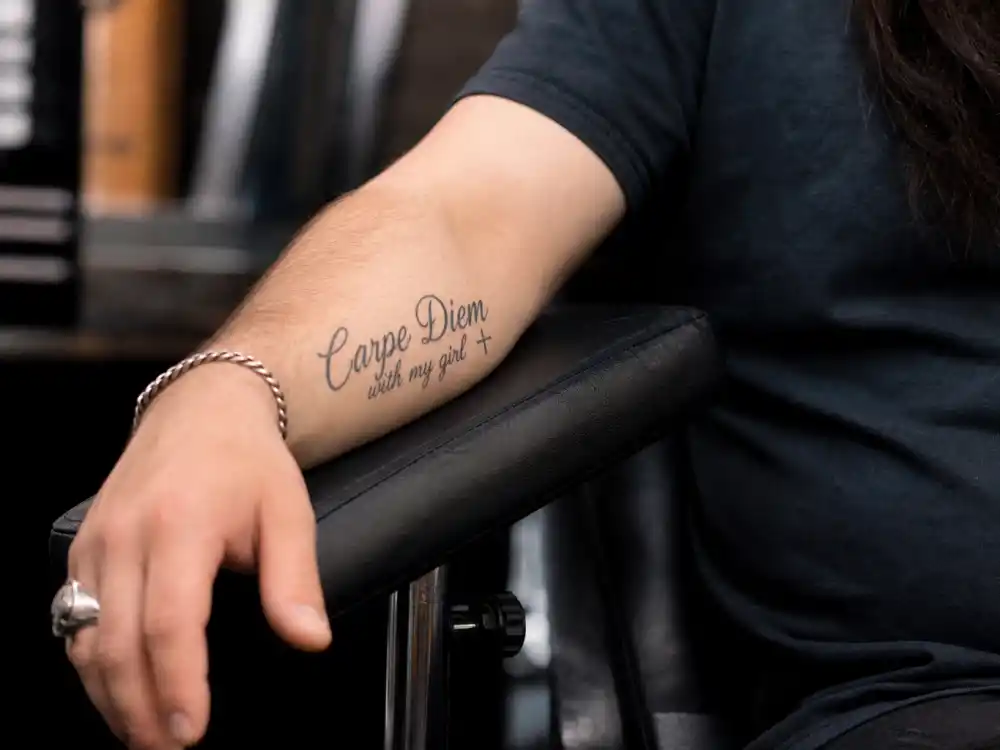 Colin Farrell tattoos and their meanings — Carpe Diem script and cross modification on left forearm close-up