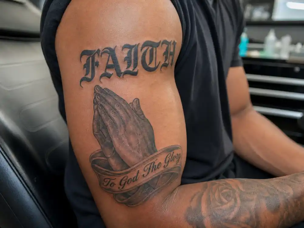 Colin Kaepernick tattoos and their meanings — FAITH bicep script and clasped prayer hands with To God The Glory banner