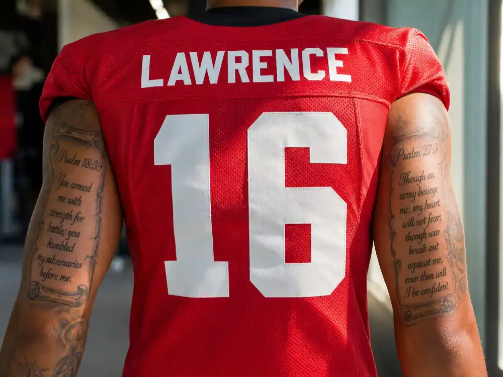 Colin Kaepernick tattoos and their meanings — Psalm 18:39 and Psalm 27:3 Bible verse scroll tattoos on both shoulders