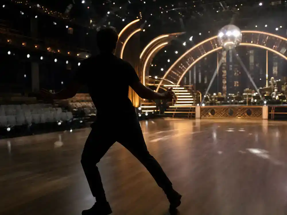 Dancing with the Stars 2026 cast guide Guillermo Rodriguez — late-night TV sidekick silhouette from behind rehearsing on ballroom competition film set