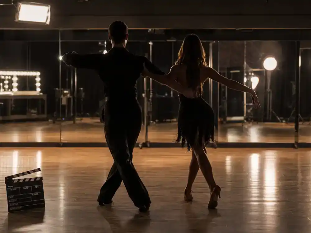 Dancing with the Stars 2026 cast guide pro dancers — professional ballroom dancer silhouettes from behind practicing in mirrored studio with TV competition lights