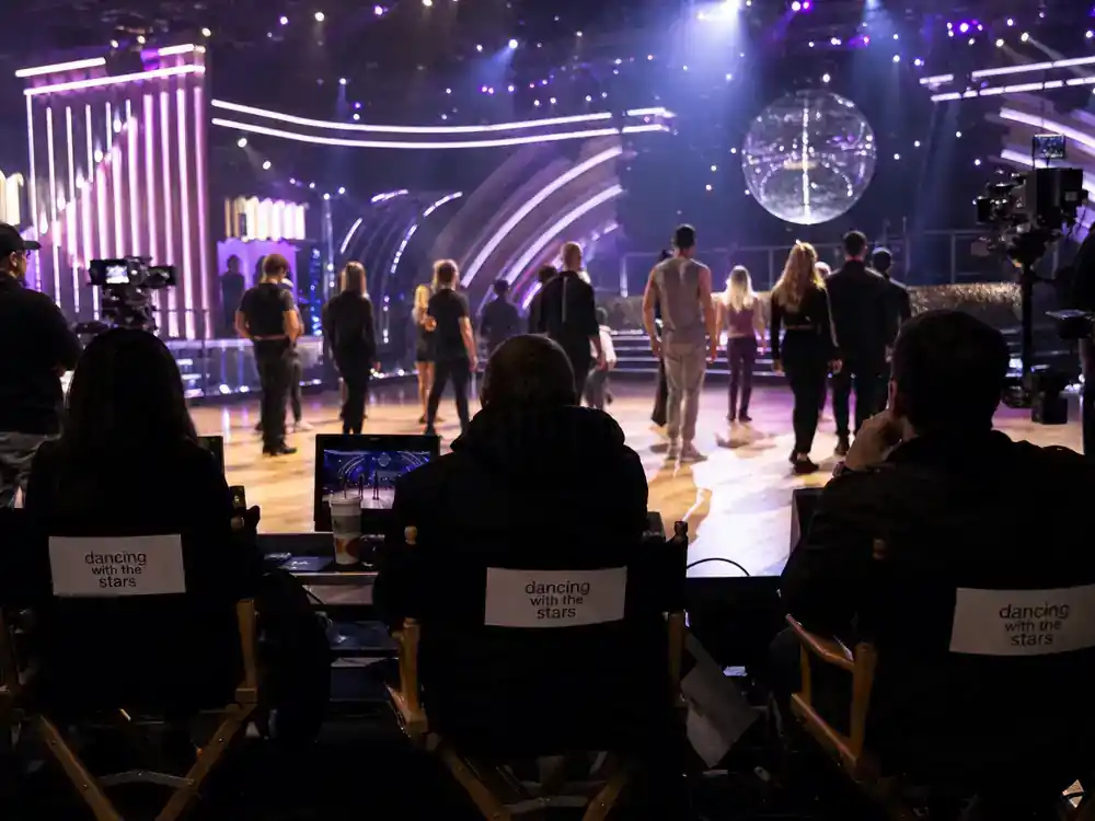 Dancing with the Stars 2026 cast guide reality stars — cast silhouettes from behind rehearsing on ballroom dance floor TV production set with director chairs