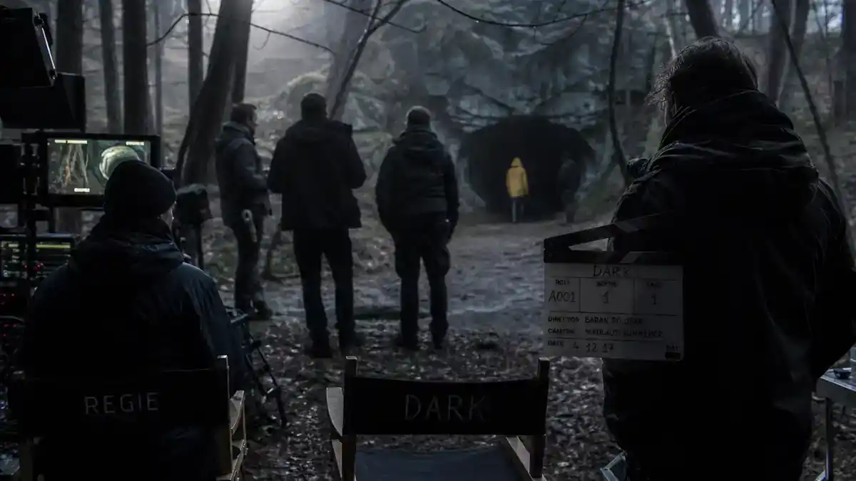 Dark Netflix cast and timeline explained — German sci-fi TV thriller production on moody forest film set with clapperboard director chairs and crew silhouettes at dusk