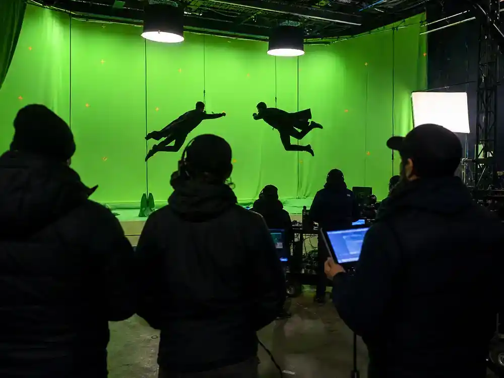 DC Universe 2026 movies and cast roadmap Superman Man of Tomorrow — actor silhouettes rehearsing wire-rig stunt on green-screen film set from behind