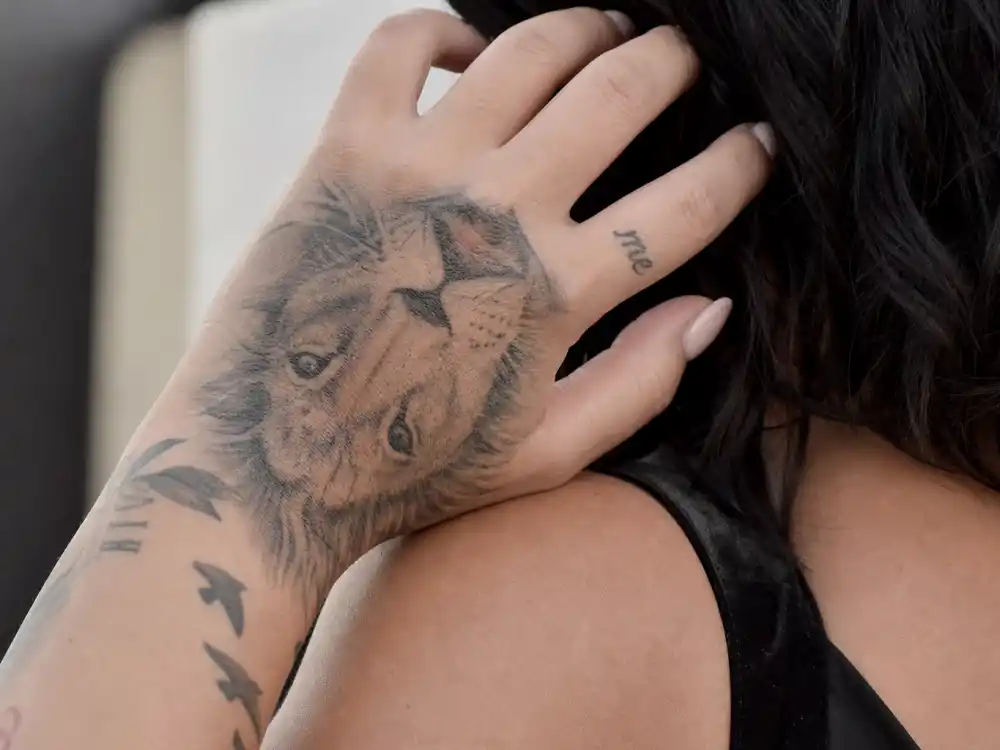 Demi Lovato tattoos and their meanings — close-up of lion face tattoo on back of hand and me script on ring finger