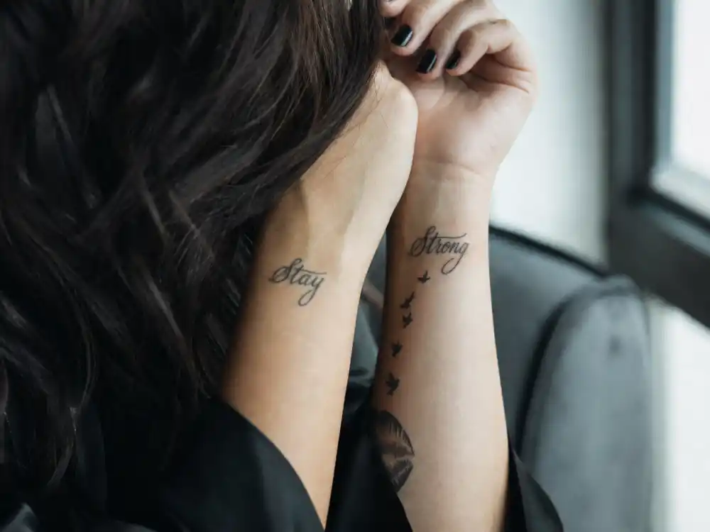 Demi Lovato tattoos and their meanings — Stay and Strong wrist tattoos with small bird silhouettes photographed in natural window light