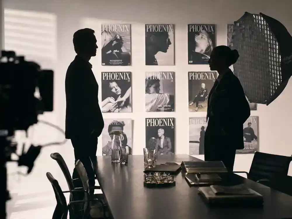 Devil Wears Prada 2 cast release date and plot Emily Charlton — two power-suited actor silhouettes in luxury brand boardroom film set, faces turned away