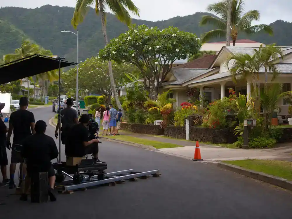 Disney live action remakes cast guide 2026 Lilo and Stitch — Hawaiian neighborhood street film location with crew silhouettes and camera dolly on family comedy set