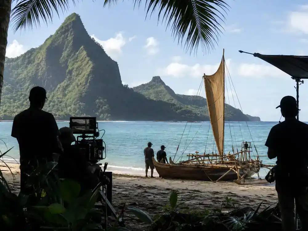 Disney live action remakes cast guide 2026 Moana — tropical ocean film set with outrigger canoe prop and crew silhouettes on beach location scout